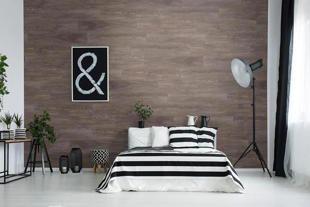 Modern bedroom with a wooden wall covering and mattress that has black and white linens