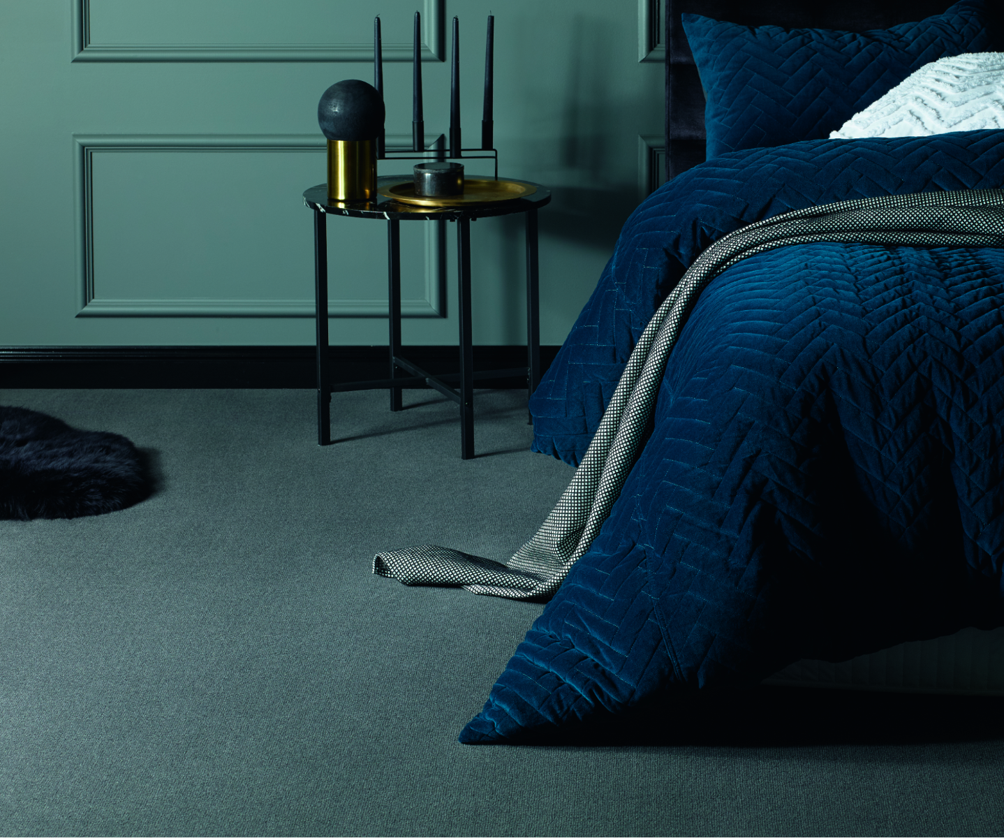 Bed with blue comforter/quilt on greyish green wool carpet