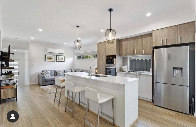 A kitchen with a timber and white design aesthetic and light fixtures to make up for the lack of windows