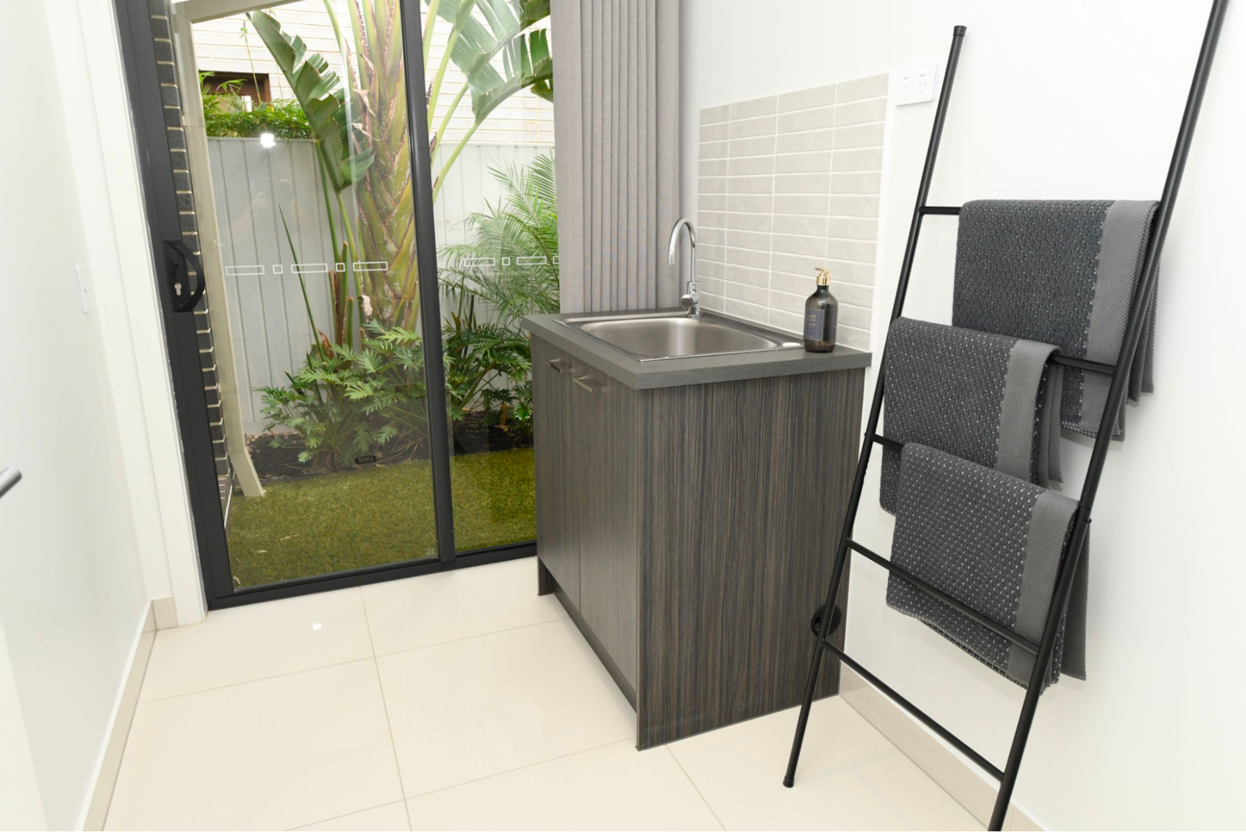 Washroom with vanity on right and splashback on its adjoining wall, sliding glass doors in the background